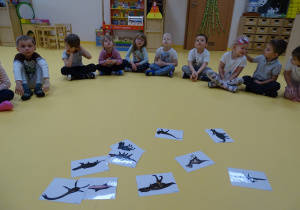 01 Dzieci siedzą w półkolu i oglądają ilustracje dinozaurów.